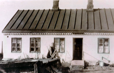Torpet från baksidan med Anna Lindros på 1920-talet. Längst ner till höger, syns  ”avloppet” som rinner ut i en hink. Fotograf okänd.