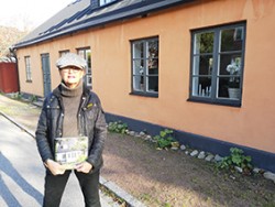 Ulla Hårde vid ett av husen i boken.